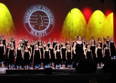 group of women in matching black dresses on stage performing at the barbershop convention