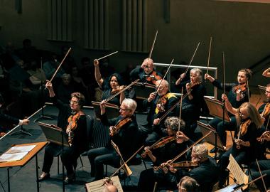 music group sitting on stage, conductor standing, ready to start the piece