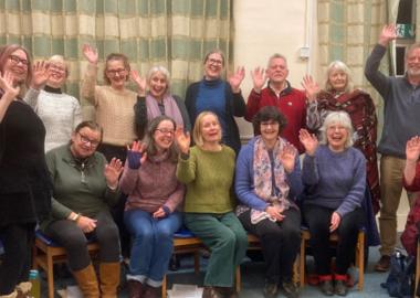 choir members, some sitting and some standing, wave and smile