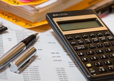 A cluttered desk with tax documents, a calculator, a pen, and a binder indicating financial calculations and tax preparation.