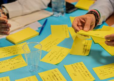 close up for people's hands over a blue table with yellow sticky notes