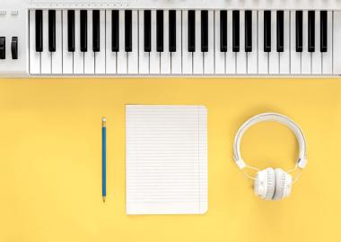 a picture of a notepad, pencil, headphones and keyboard for composing